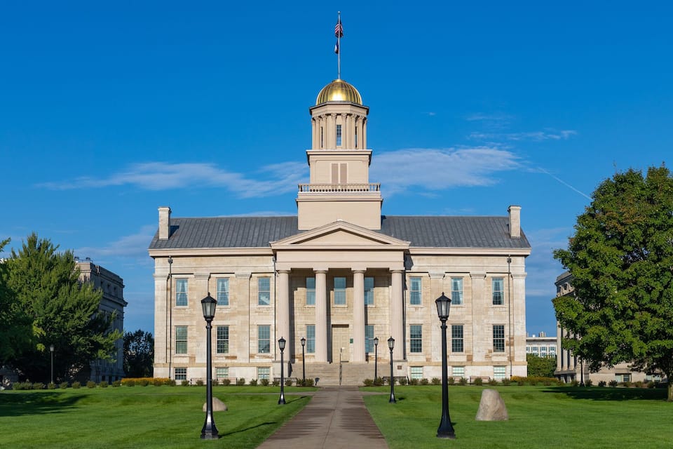 A large, historic building with a prominent dome and columns, surrounded by well-maintained lawns and trees.