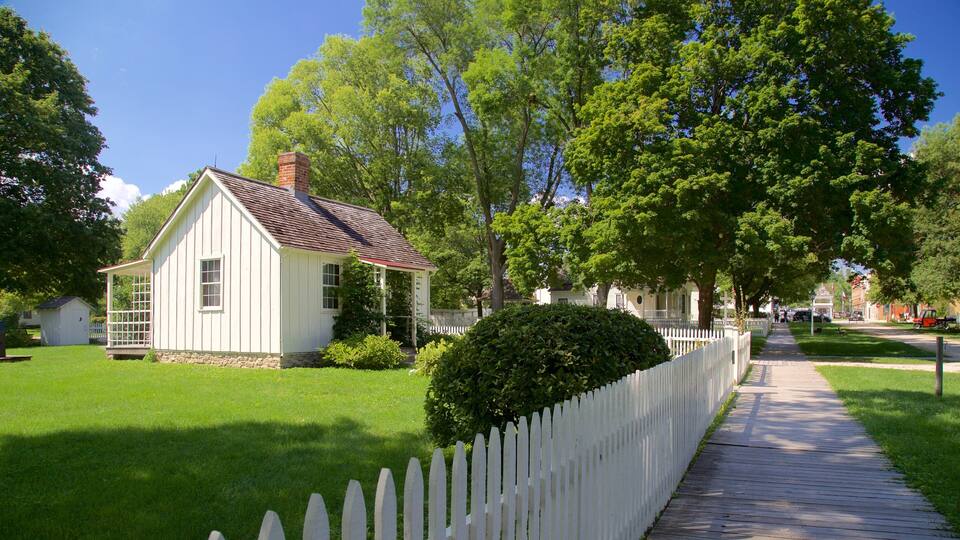 A white wooden house with a red roof, surrounded by lush green trees and a white picket fence.