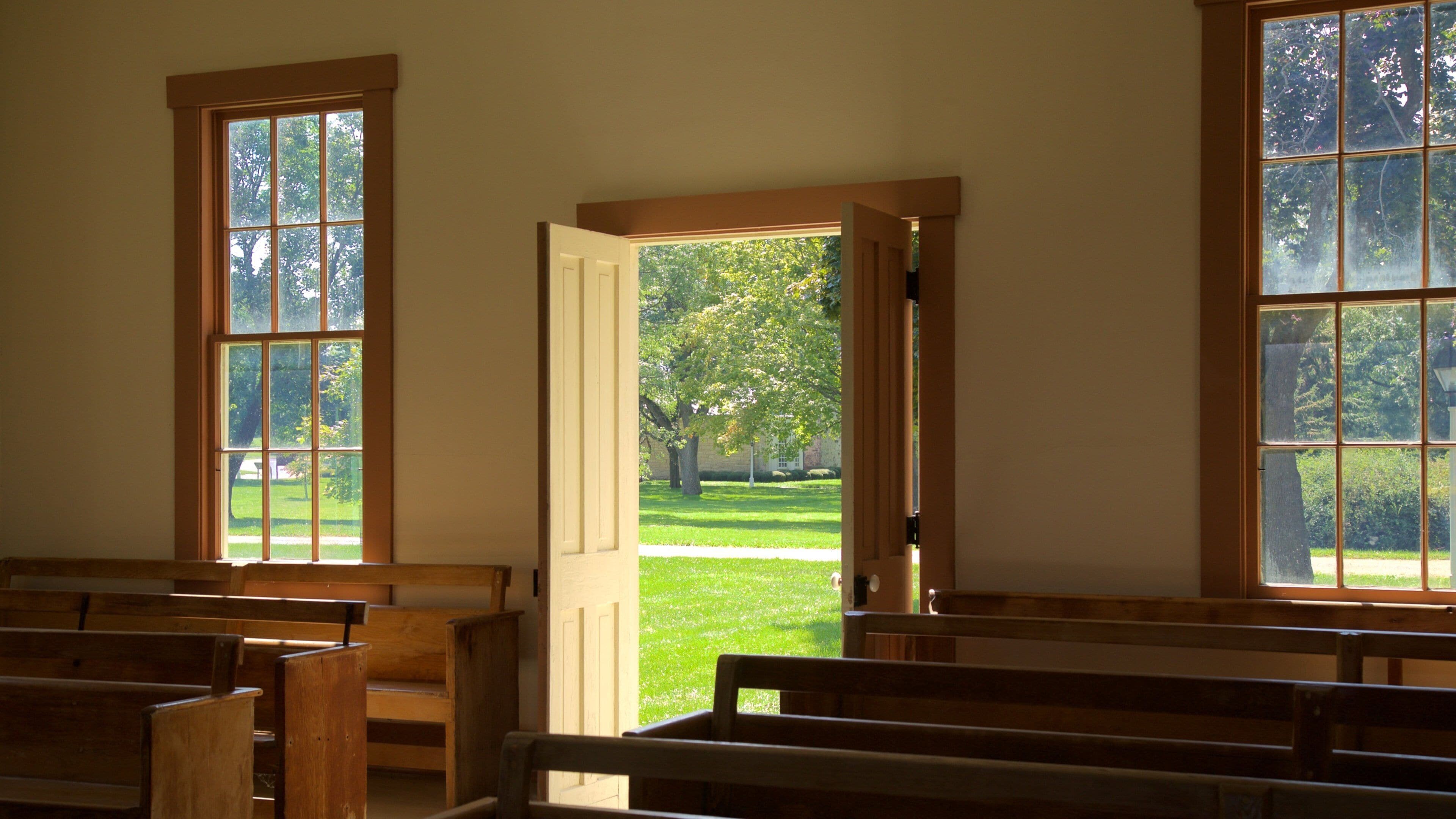 A church interior with wooden pews and large windows.