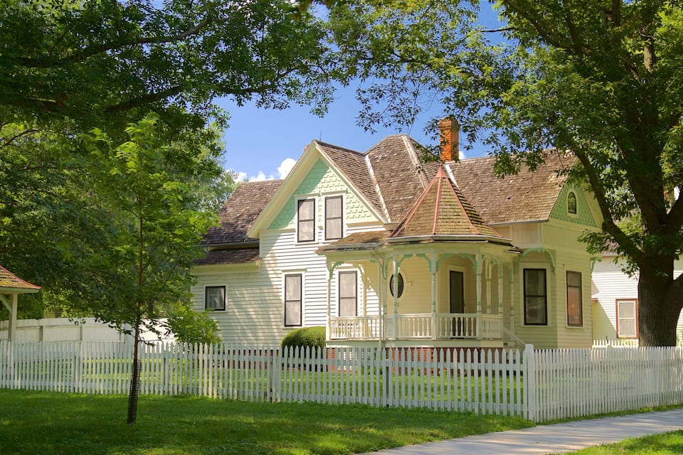 A historic house with a white picket fence, surrounded by lush greenery and trees.