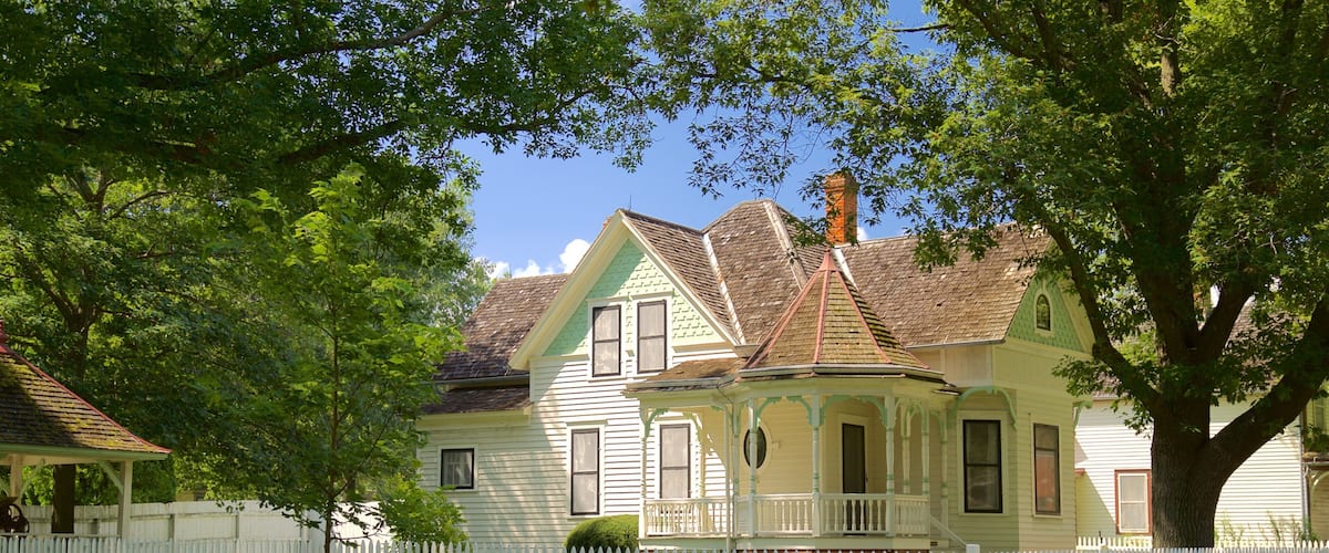 A historic house with a white picket fence, surrounded by lush greenery and trees.