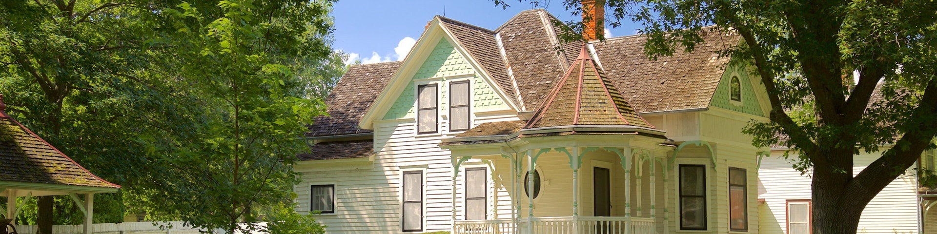 A historic house with a white picket fence, surrounded by lush greenery and trees.