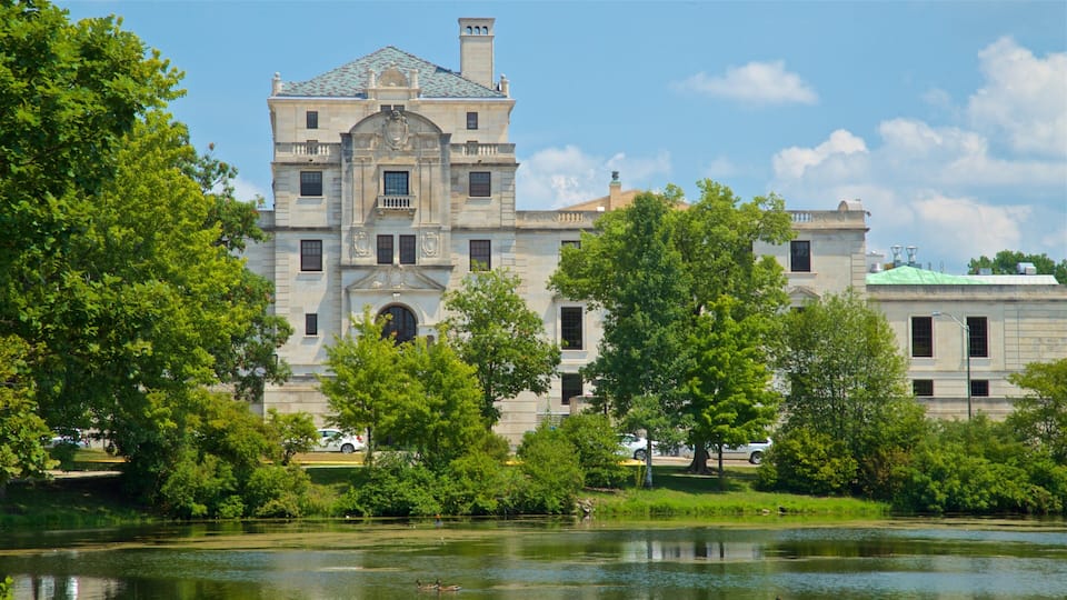 A historic building with a large central archway and a pond in the foreground.