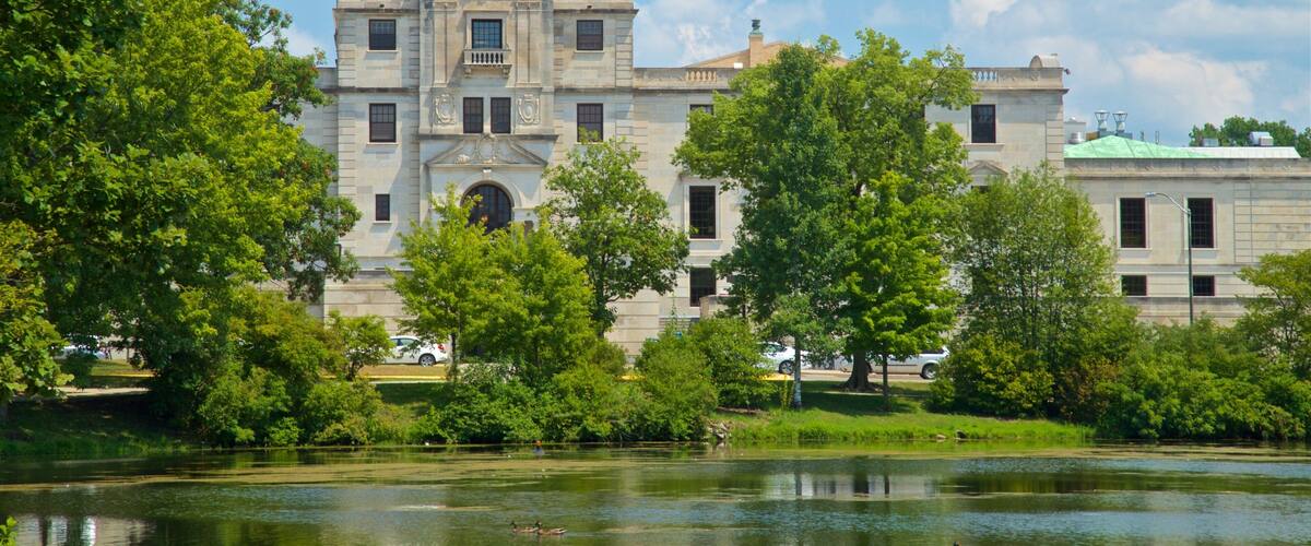 A historic building with a large central archway and a pond in the foreground.