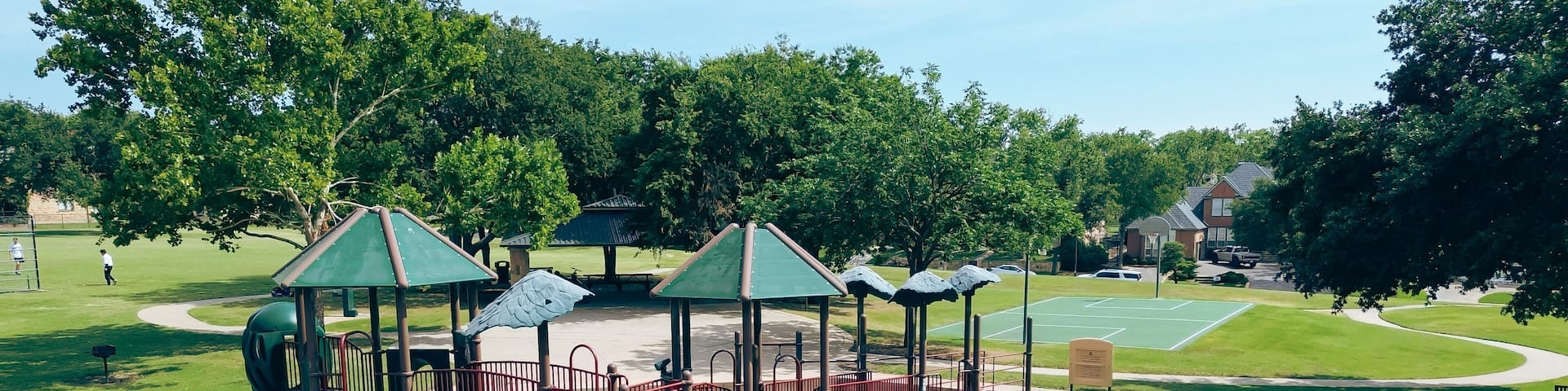 People playing baseball softball near backstop netting in grassy community park with modern playground equipment, hopper fun bouncer string rider, basketball court, upscale house, Plano, aerial