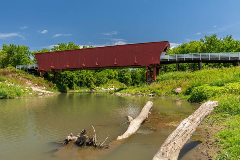 A red bridge over a calm river with greenery around.