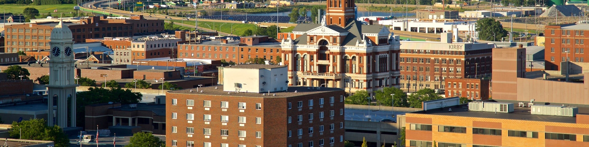 A cityscape with a prominent clock tower, a large red building with a dome, and a river in the background.