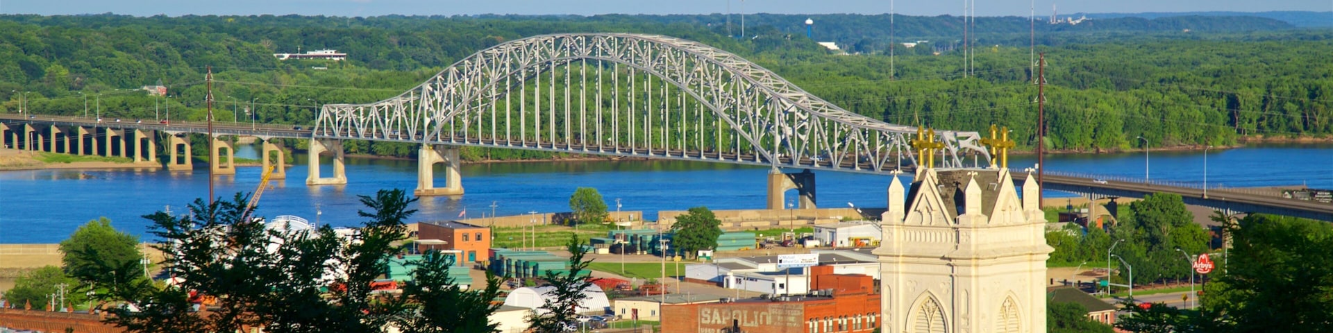 Un puente arco de acero sobre un río, rodeado de vegetación y edificios.