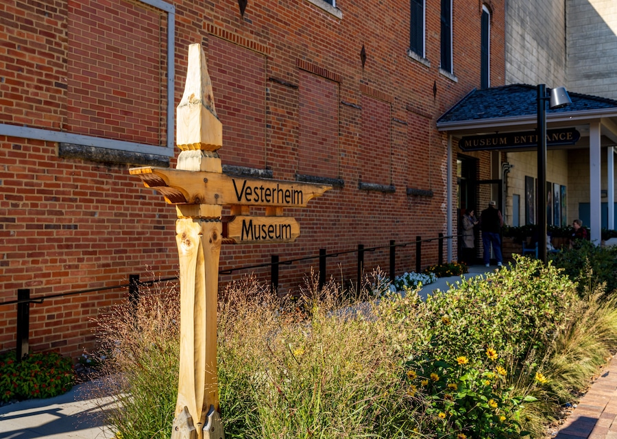 Un cartel de madera con la inscripción 'Vesterheim Museum', frente a un edificio de ladrillo con un letrero que dice 'Entrada al Museo'.