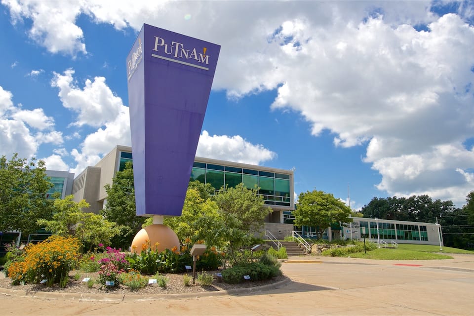 A tall purple sign with the text "PUTNAM" in front of a modern building with glass windows.