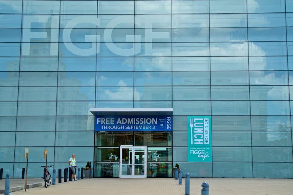 A modern building facade with large glass windows and a blue sign advertising free admission through September 3.