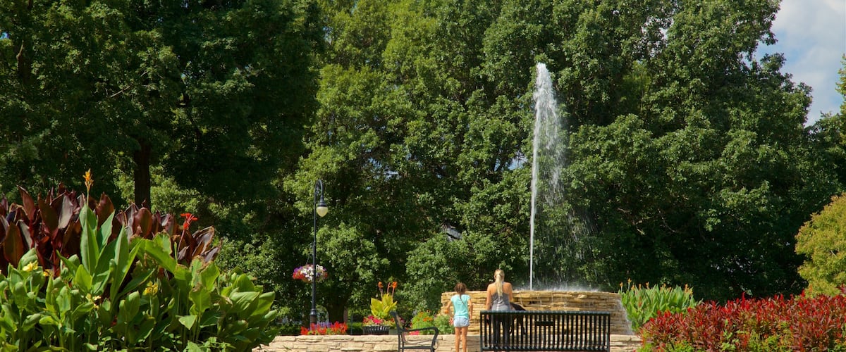 A park with a fountain, lush greenery, and a stone wall.