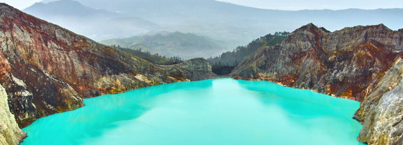 Un lago turquesa rodeado de terreno volcánico escarpado y multicoloreado.