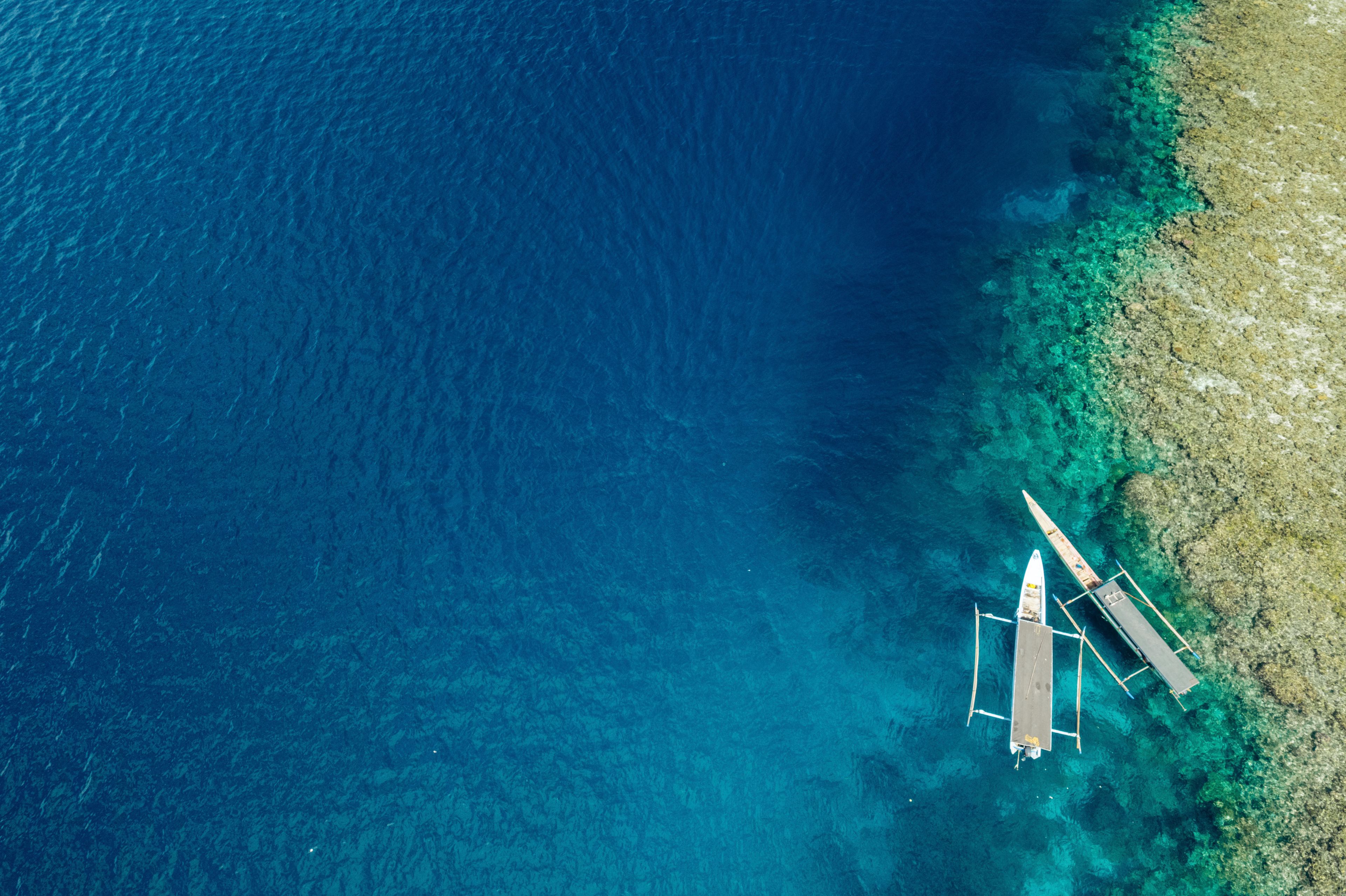 An aerial view of a clear blue sea with a sandy beach and two traditional boats anchored near the shore.