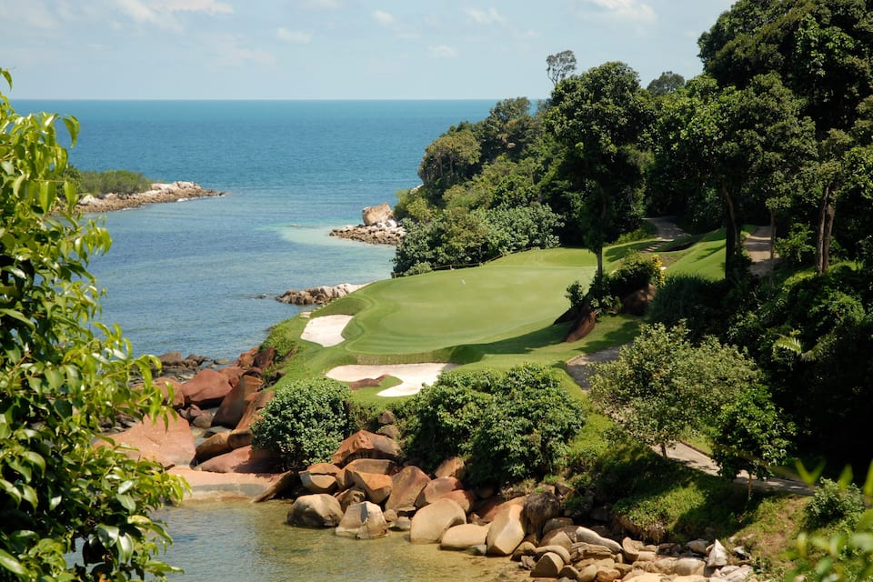 Un parcours de golf situé sur la côte, offrant une vue dégagée sur l’océan, et entouré d’une végétation luxuriante et d’un paysage rocheux.