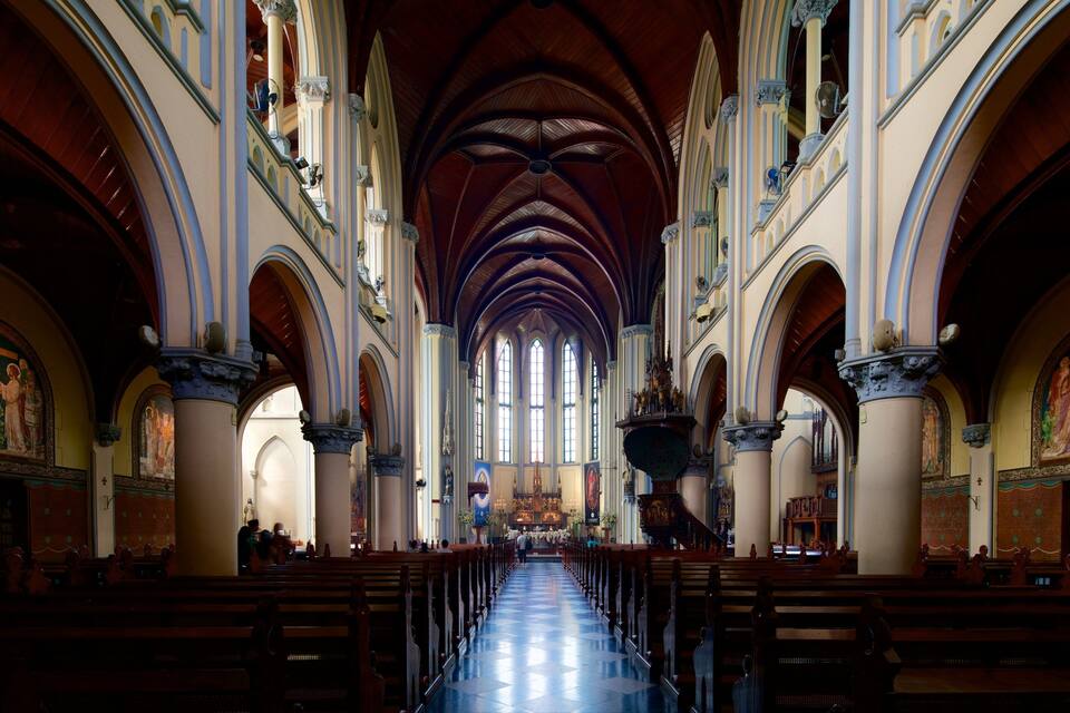 Interior de uma igreja com tetos abobadados altos, fileiras de bancos e vitrais.