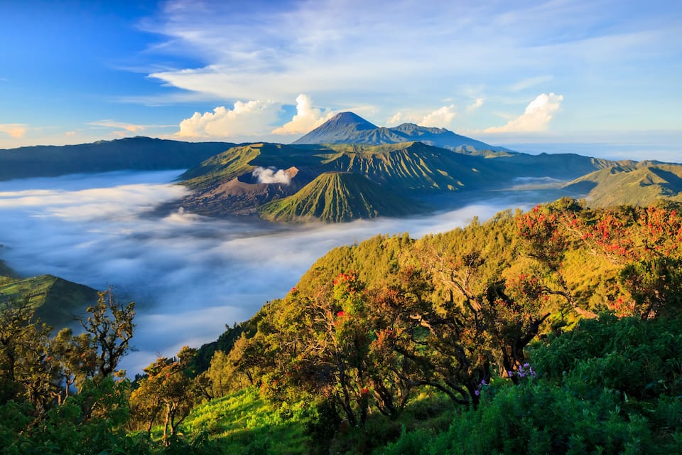 Una montaña con una capa de nubes, rodeada de colinas boscosas.