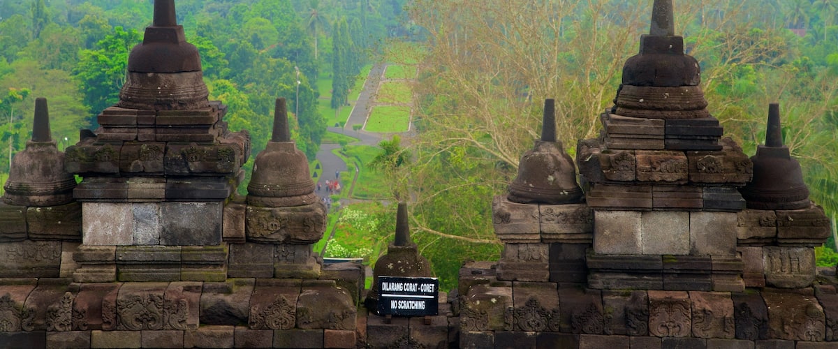 Ancient stone structures with pointed tops and a sign indicating 'Dilarang Corat - Coret No Scratching'.