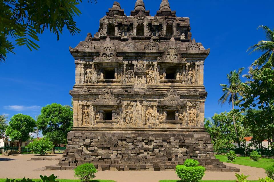 Un templo de piedra detallado con intrincados grabados, rodeado de exuberante vegetación y palmeras.