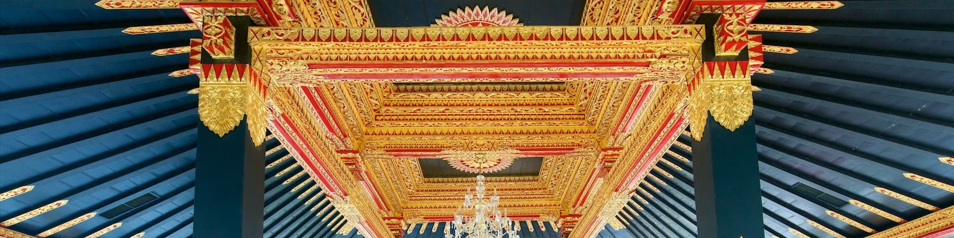 An ornate architectural structure with intricate golden and red patterns, a central floral motif, and a chandelier.