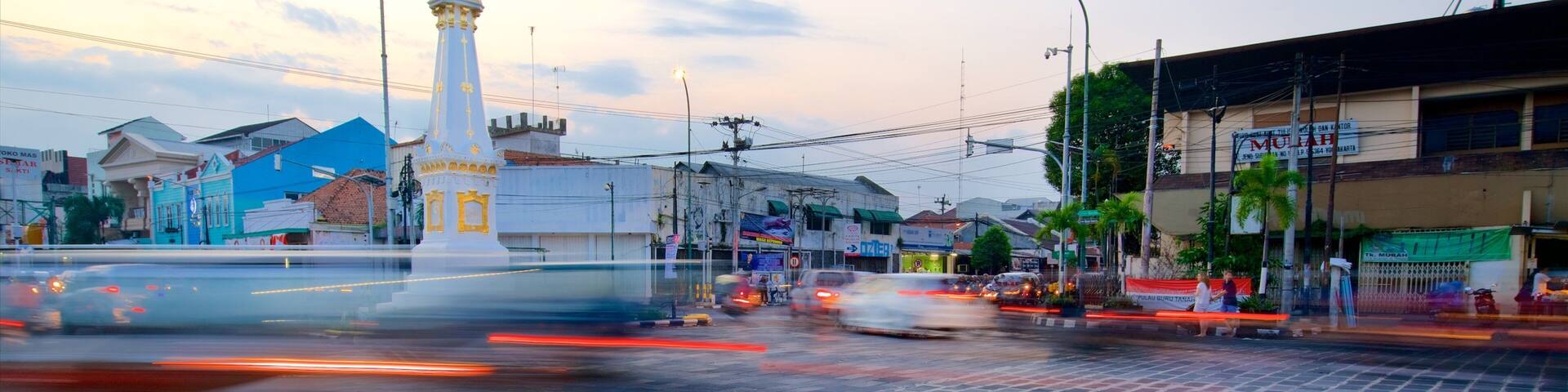 A busy urban intersection with a prominent white monument, various buildings, and a clear sky.