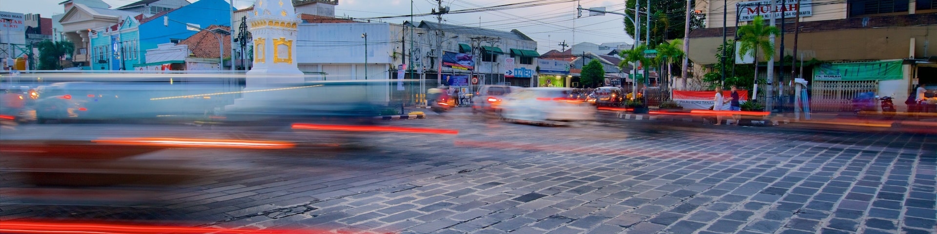 Um movimentado cruzamento urbano com um monumento branco imponente, vários edifícios e céu limpo.