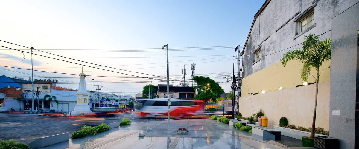 A wet urban street with a white building, a red car, and a white van.