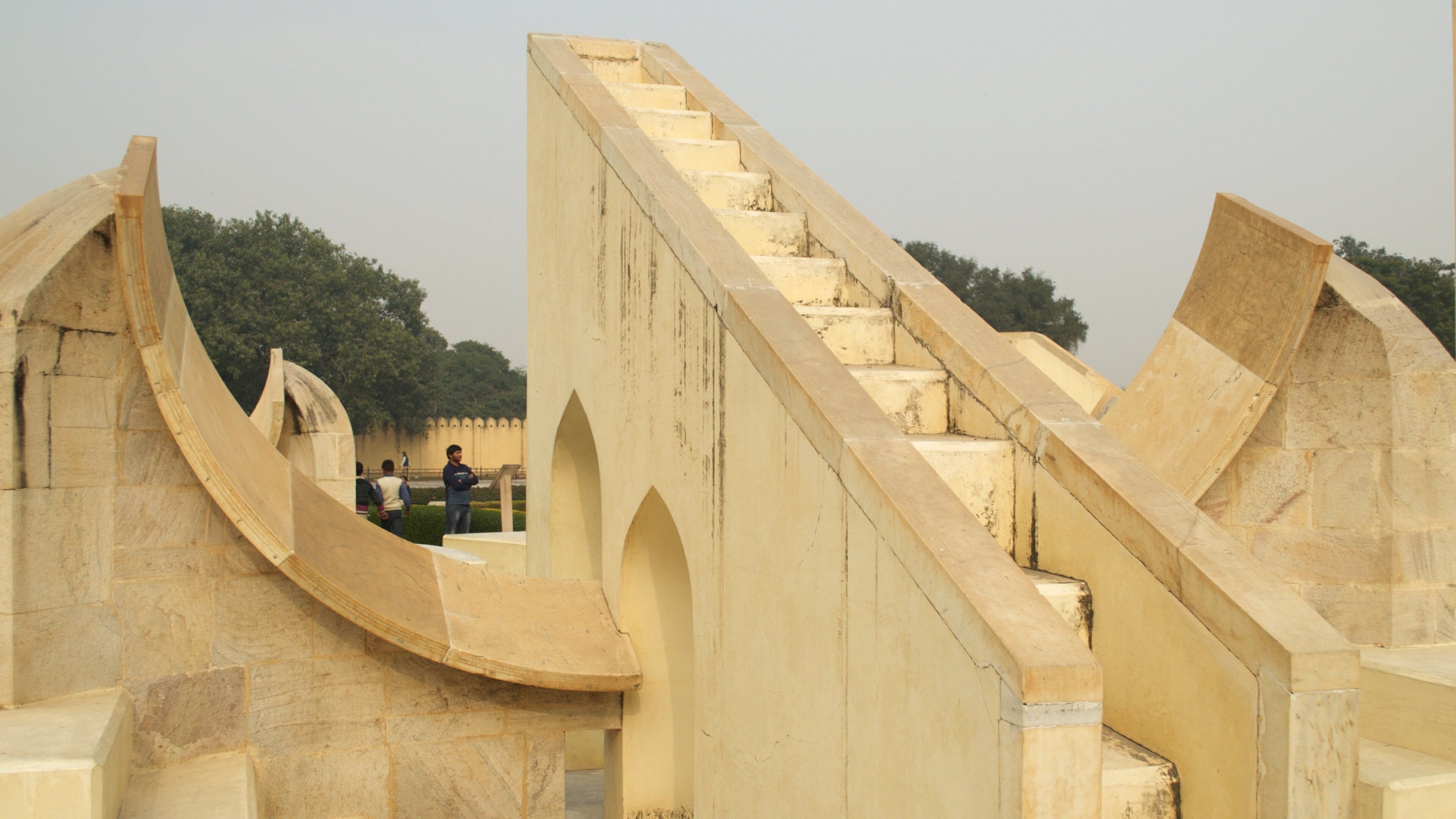 A stone staircase with arches, surrounded by stone walls and trees.
