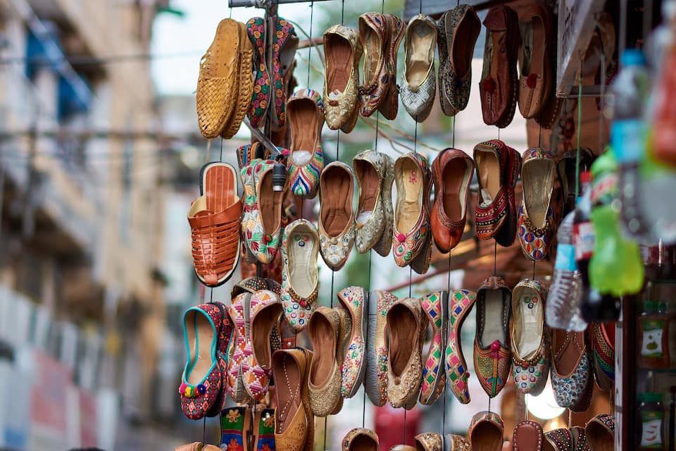 Diversos sapatos coloridos e ricamente detalhados pendurados em uma estante.