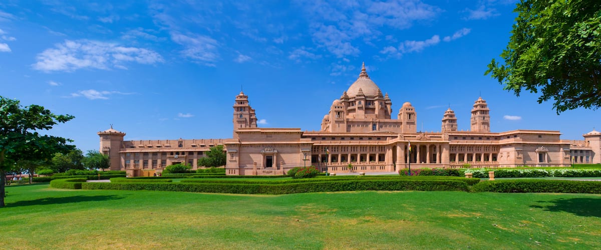 A large, historic building with multiple towers and domes, surrounded by well-maintained lawns and trees.