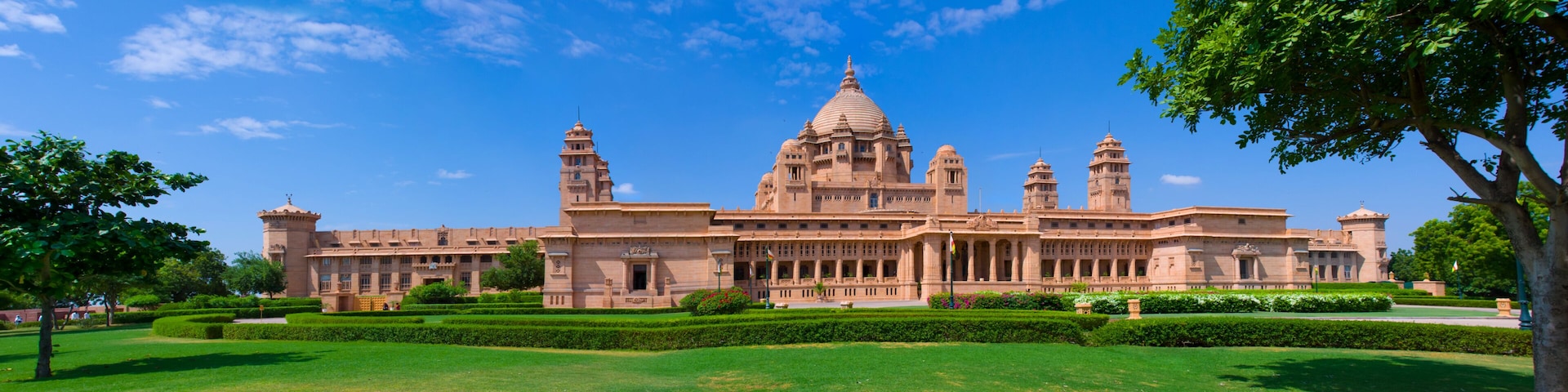 A large, historic building with multiple towers and domes, surrounded by well-maintained lawns and trees.