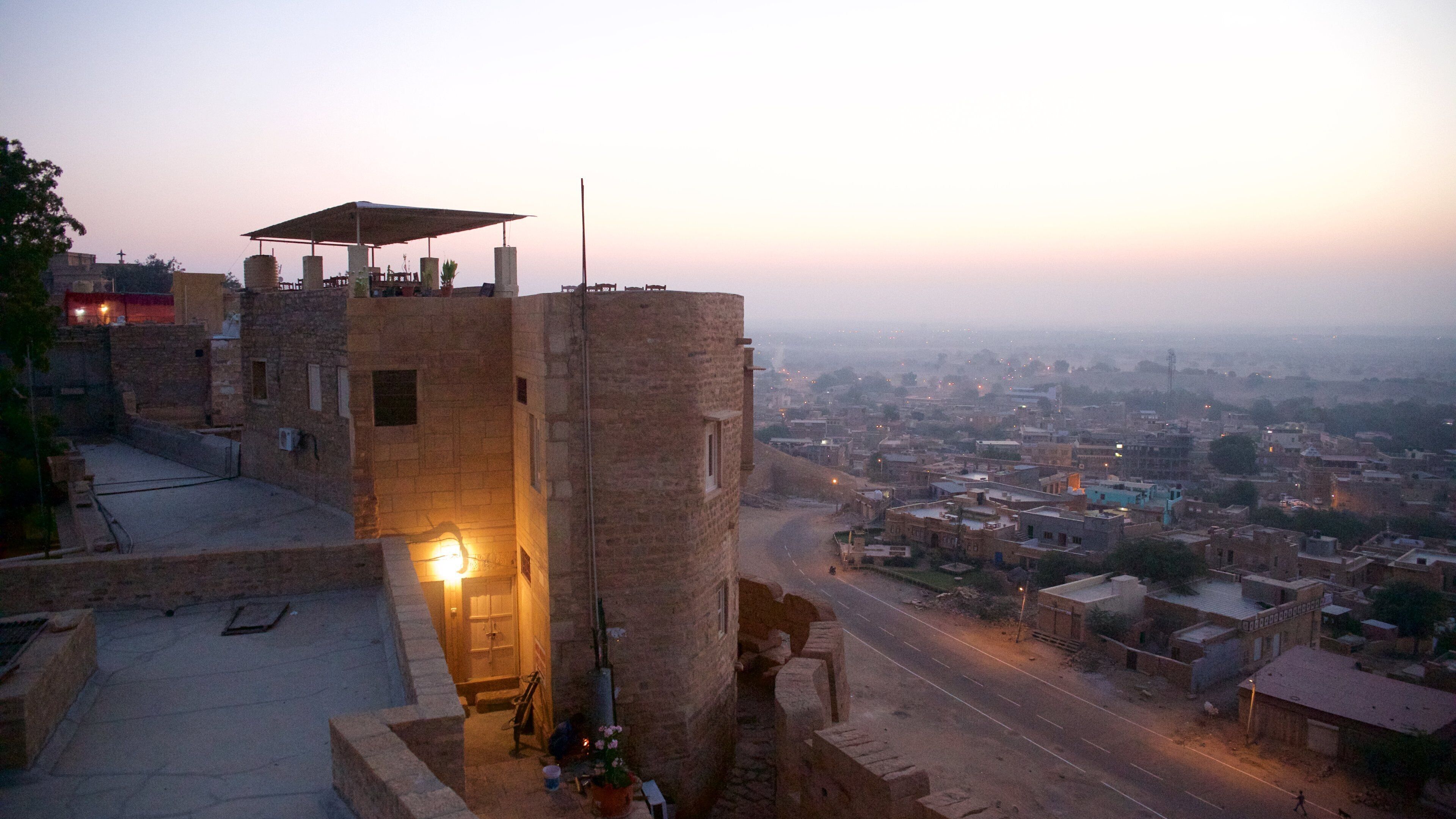 A historic stone tower with a lit lantern, overlooking a cityscape at dusk.