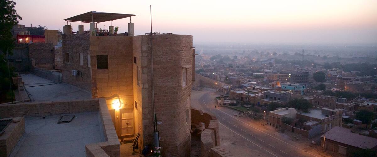 A historic stone tower with a lit lantern, overlooking a cityscape at dusk.