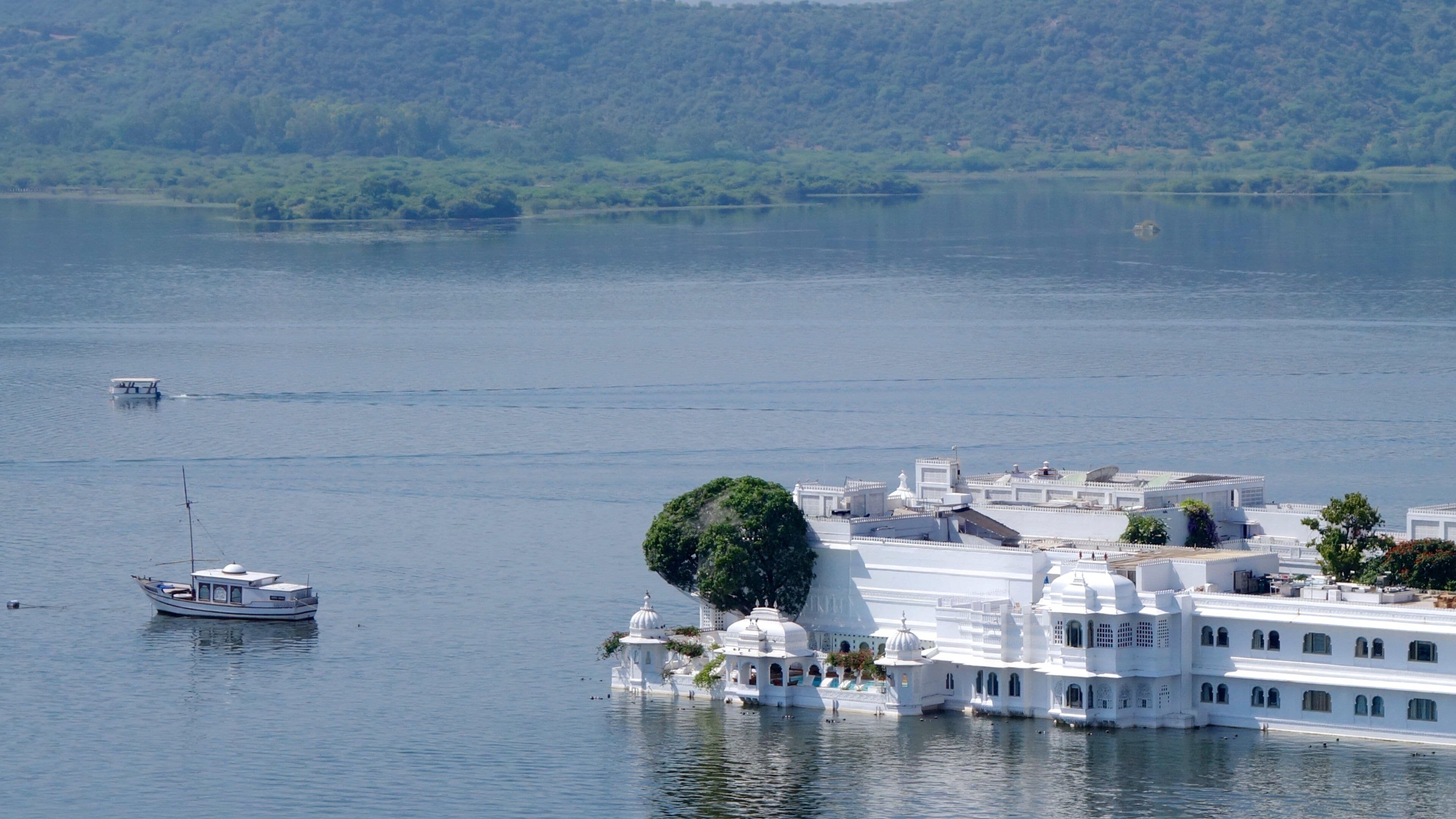 Ein weißes Gebäude mit Kuppeln und einem Baum an einem See, der von Hügeln umgeben ist.
