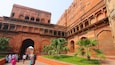A historic building with arches and columns, palm trees, and people in traditional attire.