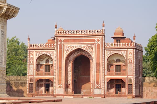 A Mughal-style building with intricate white and red patterns, arched doorways, and a dome.