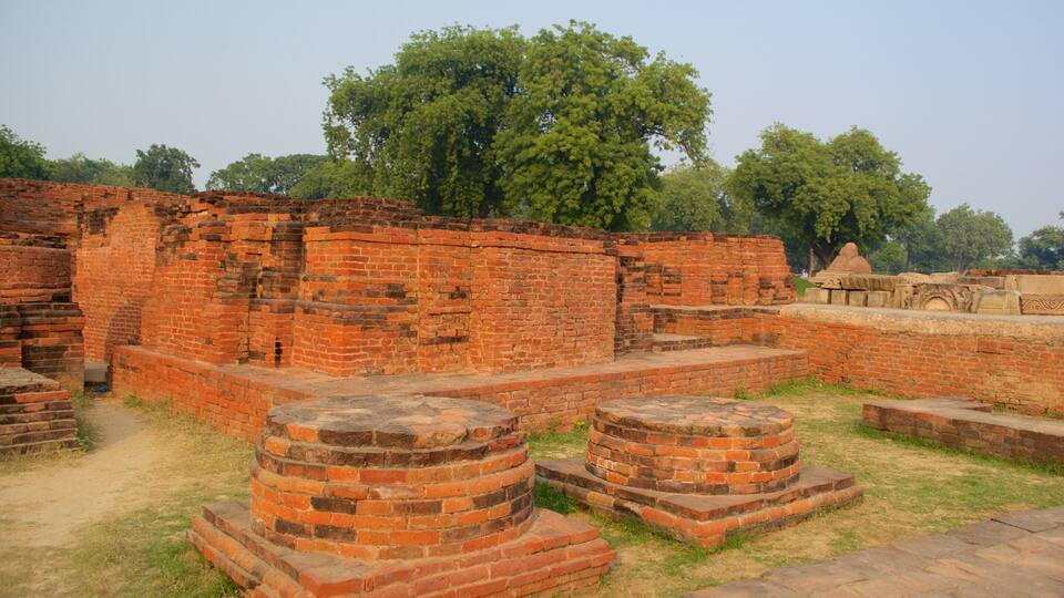 Ancient brick ruins with circular stone structures, surrounded by trees.