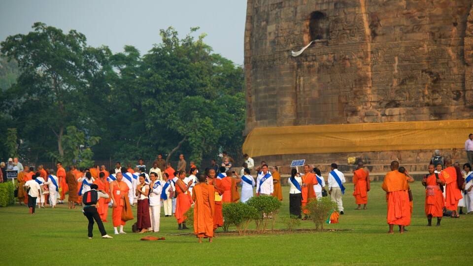 A group of monks in orange robes gathered in a grassy area with a large stone structure in the background.