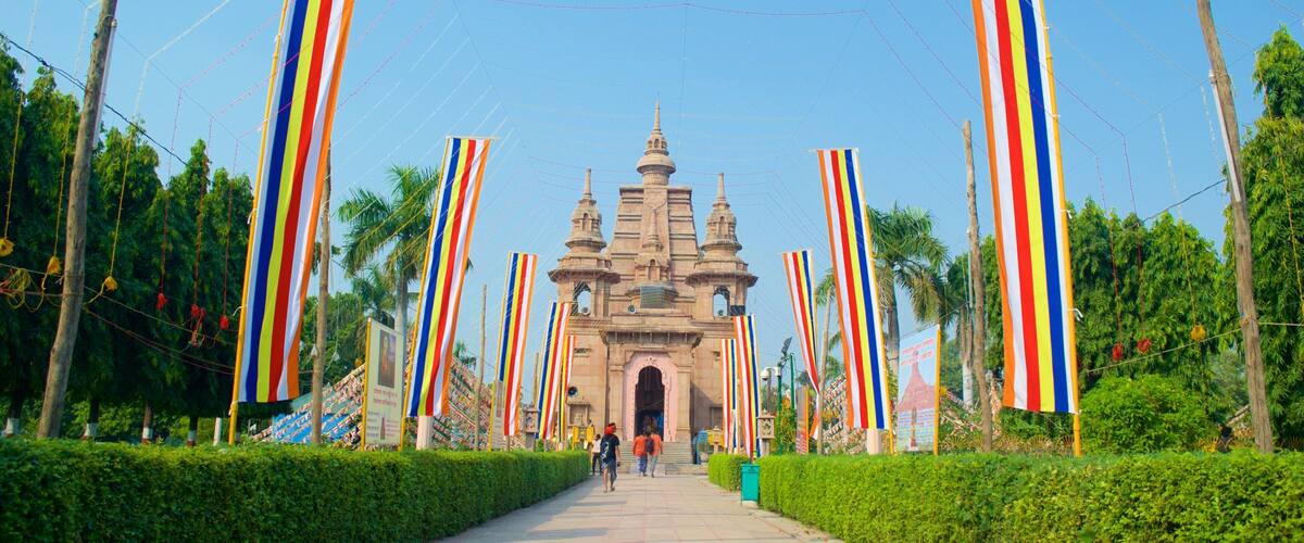 A historic temple with a central entrance flanked by colorful flags, surrounded by lush greenery.