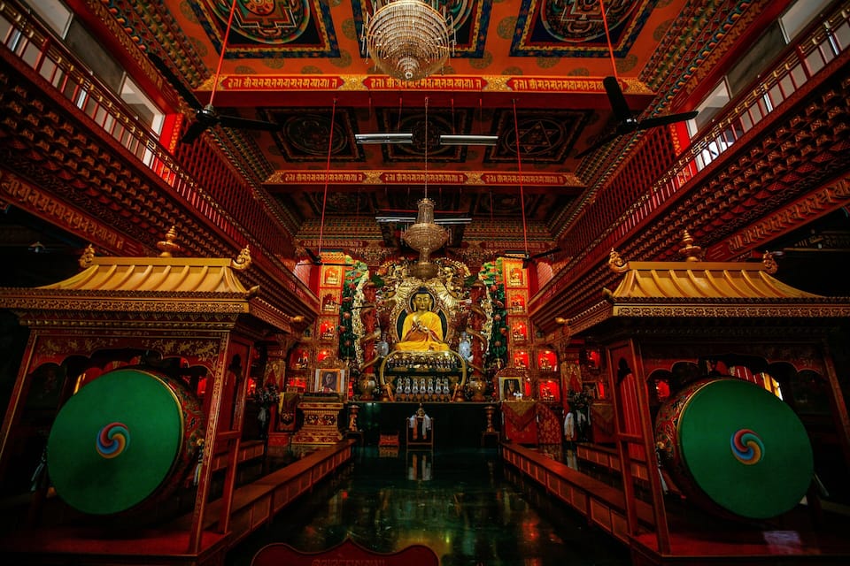 An ornate temple interior with a central statue, intricate carvings, and a chandelier.