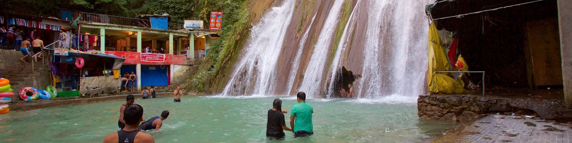 A waterfall in a forested area with people in the water and a building nearby.