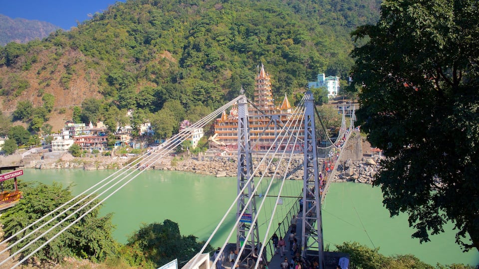 A suspension bridge over a river with buildings and trees in the background.