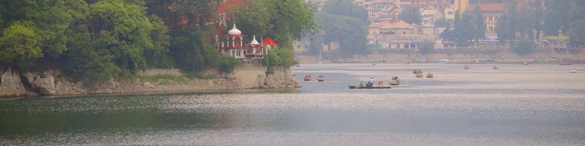Un río con barcos, un templo en un acantilado y una ladera con construcciones apretadas al fondo.