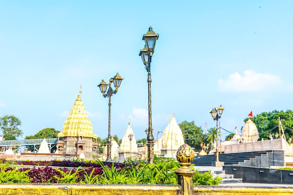 A temple complex with golden spires, ornate street lamps, and lush greenery.