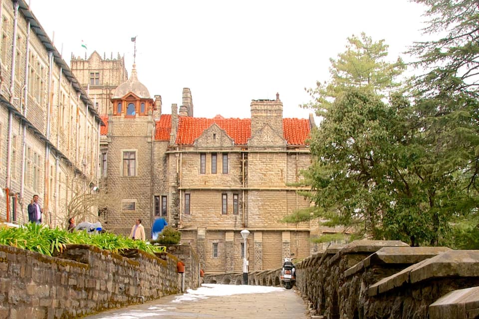A historic stone building with red-tiled roofs, a narrow stone pathway, and a tree-lined street.