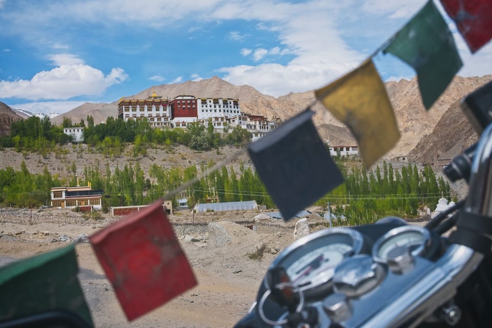 A motorcycle with flags in the foreground, a building with a golden dome, and a mountainous landscape in the background.