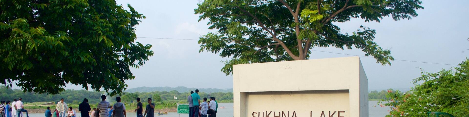 A sign for Sukhna Lake with people walking nearby.