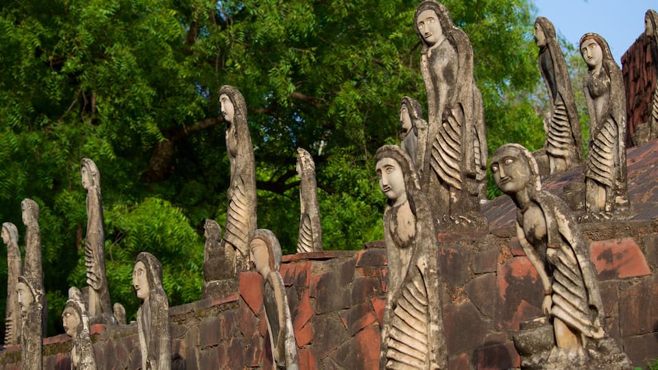 A collection of stone statues with skeletal features, set against a backdrop of lush green trees.