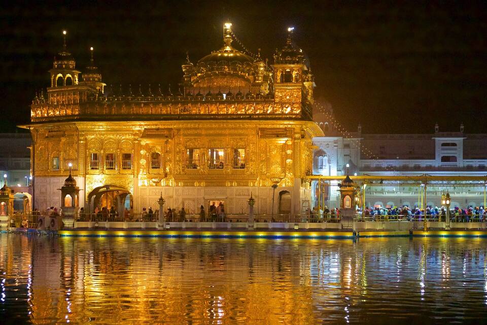 A brightly lit golden temple at night with reflections in the water.