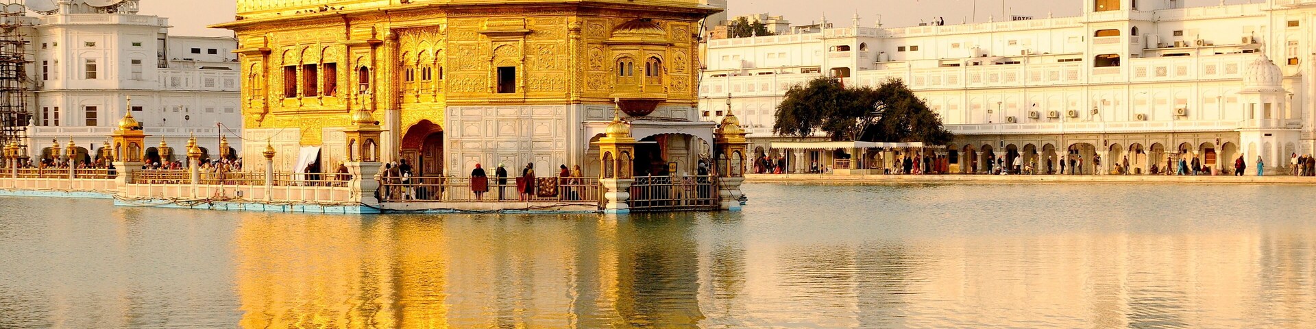 O Templo Dourado com seu reflexo na água, rodeado por edifícios brancos.